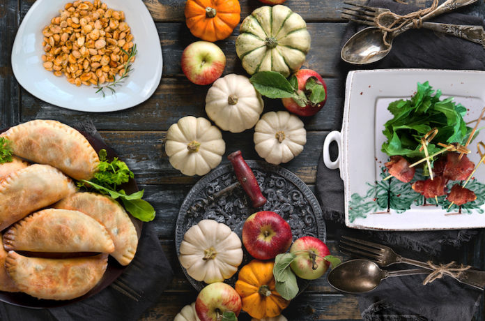 Holiday table decoration Autumn holiday recipes dishes set with decorative pumpkins, apples, red leaves with vintage cutlery, red wine, candle over wooden table. Rustic style.